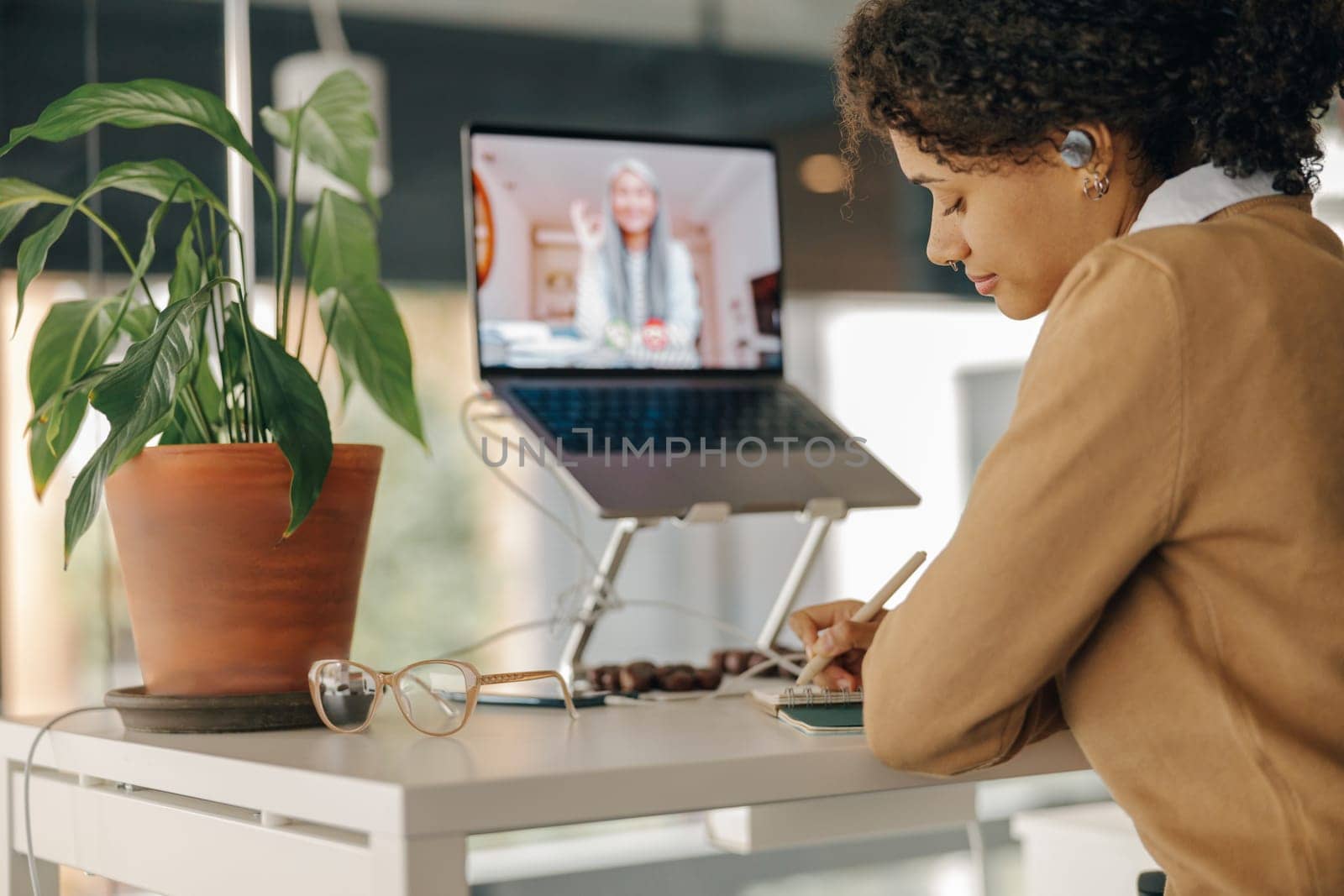 Female freelancer have video conference with client and making notes sitting in cozy coworking
