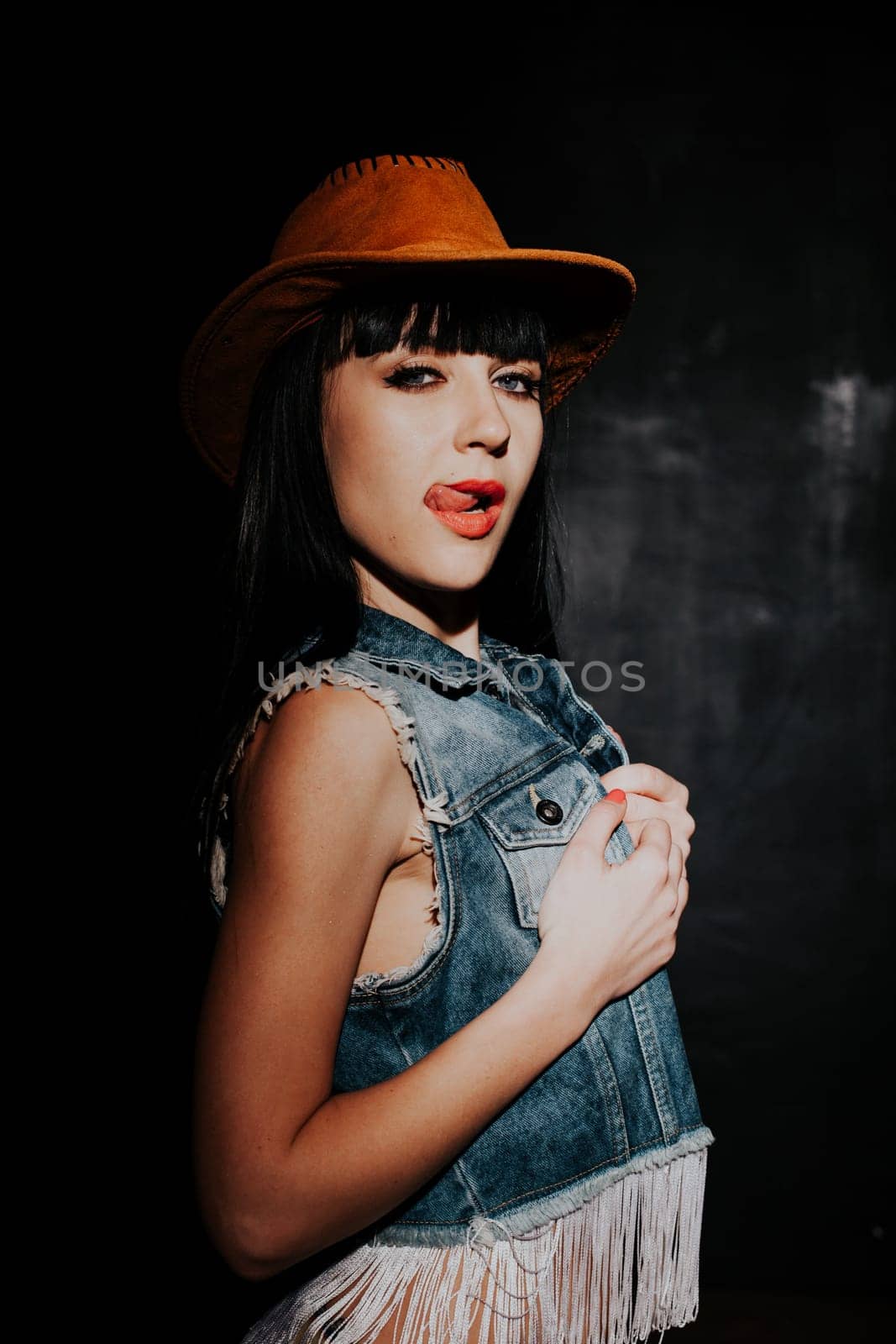 beautiful sexy girl in cowboy hat and denim waistcoat on a black background