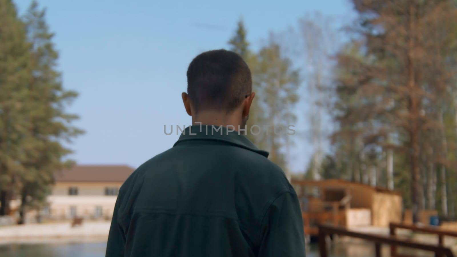 Man walks along resort in forest. Stock footage. Place to relax in nature in forest on sunny summer day. Man walks through recreation center in forest with lake.