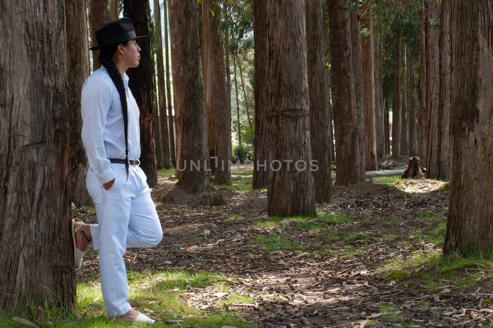 horizontal photo with copyspace of an ecuadorian indian with white clothes and a long braid to the waist with a black hat looking at the horizon full of trees. hair day. by Raulmartin