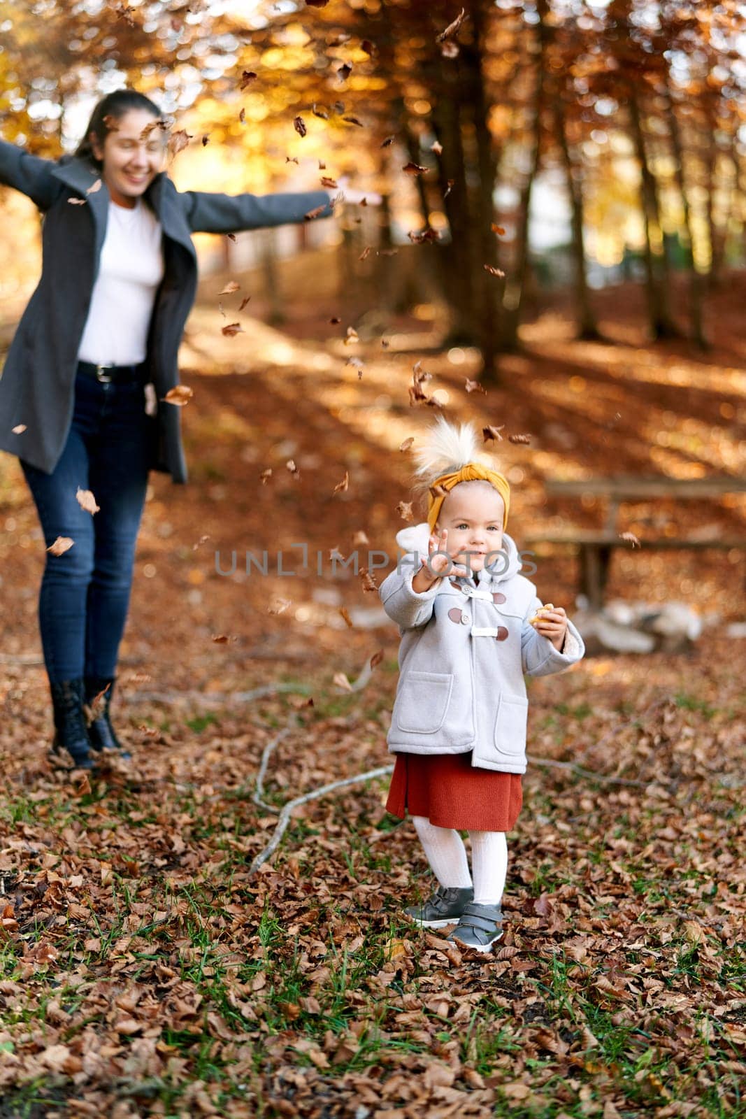 Laughing mother throws up fallen leaves on a little girl in the autumn forest. High quality photo