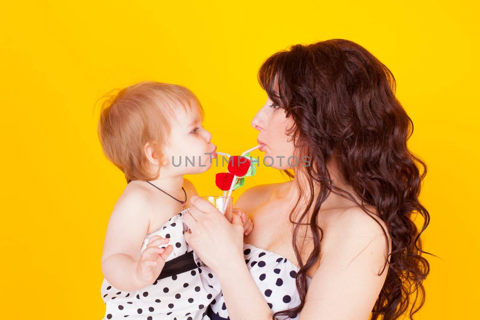 mother and little daughter drunk from drinking straws cocktail on a yellow background