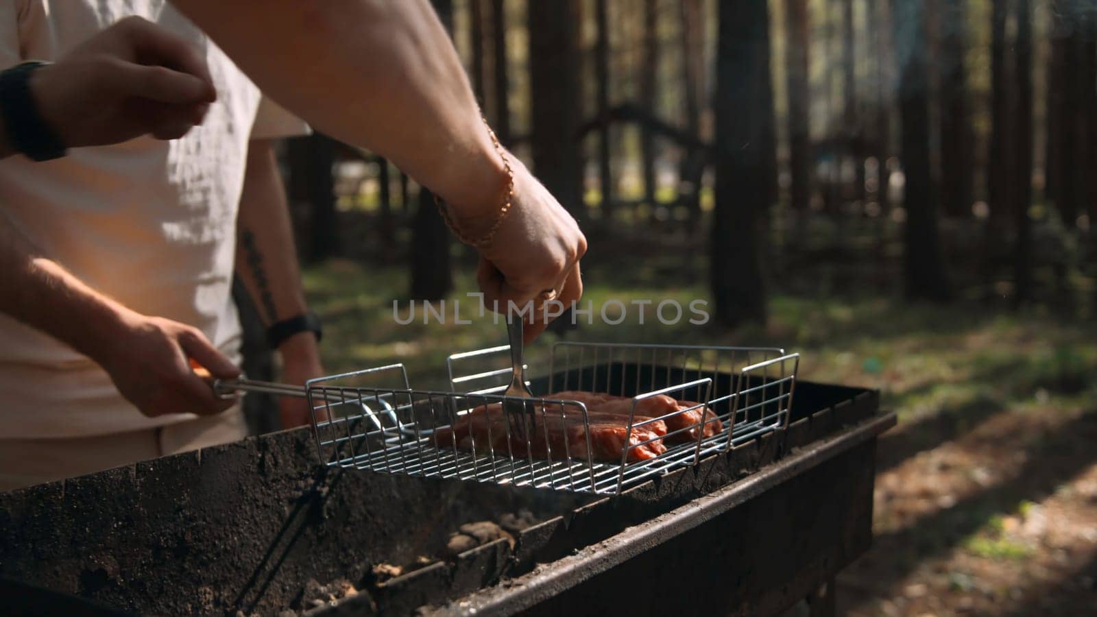 Close-up of men frying chicken on grill in forest. Stock footage. Delicious grilled chicken with barbecue on sunny summer day. Men cook chicken on grill and relax in forest.