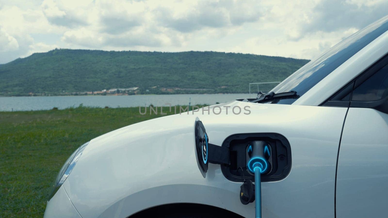 Electric car plugged in with charging station with nature background. Peruse by biancoblue