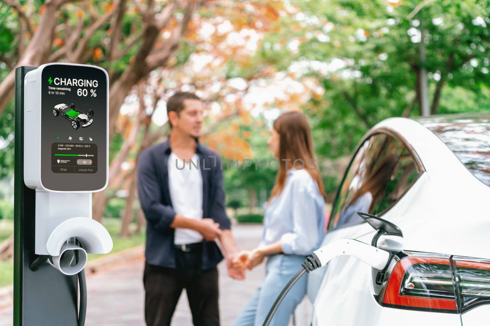 Lovely young couple recharging battery for electric car in autumn. Exalt by biancoblue