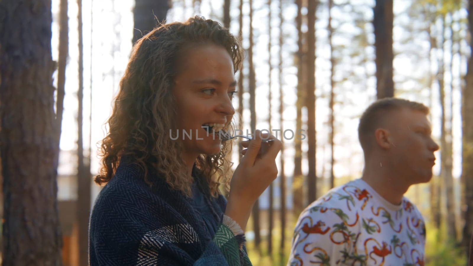 Group of friends eats vegetables at grill in nature. Stock footage. Beautiful friends have fun chatting at barbecue in forest. Fun vacation with friends in forest on sunny summer day.