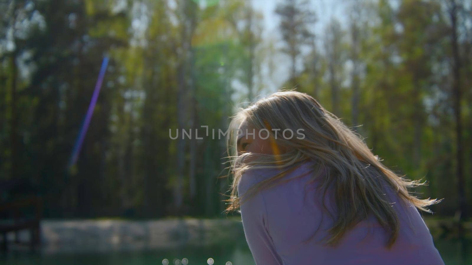 Beautiful young woman on sunny summer forest background. Stock footage. Beautiful blonde woman on background of sunlight and summer forest. Portrait of sitting woman in sunny forest.