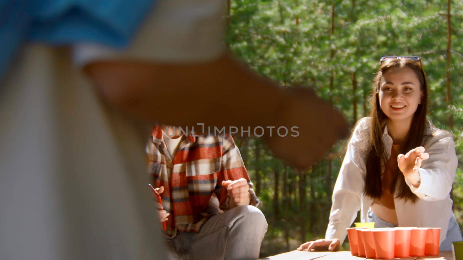 Beer pong with friends. Stock footage. Beautiful young woman playing beer pong with friends. Beer pong game in nature on summer day.