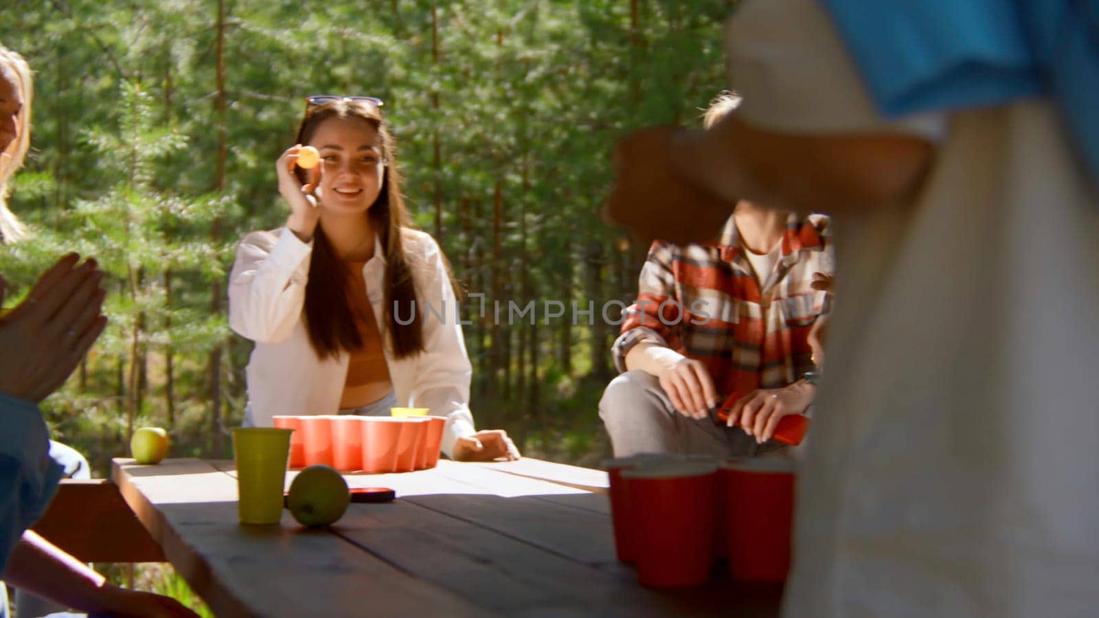 Young woman playing beer pong. Stock footage. Beautiful woman throws ball into glass of beer. Fun game for friends with alcohol and ping pong in nature in summer.