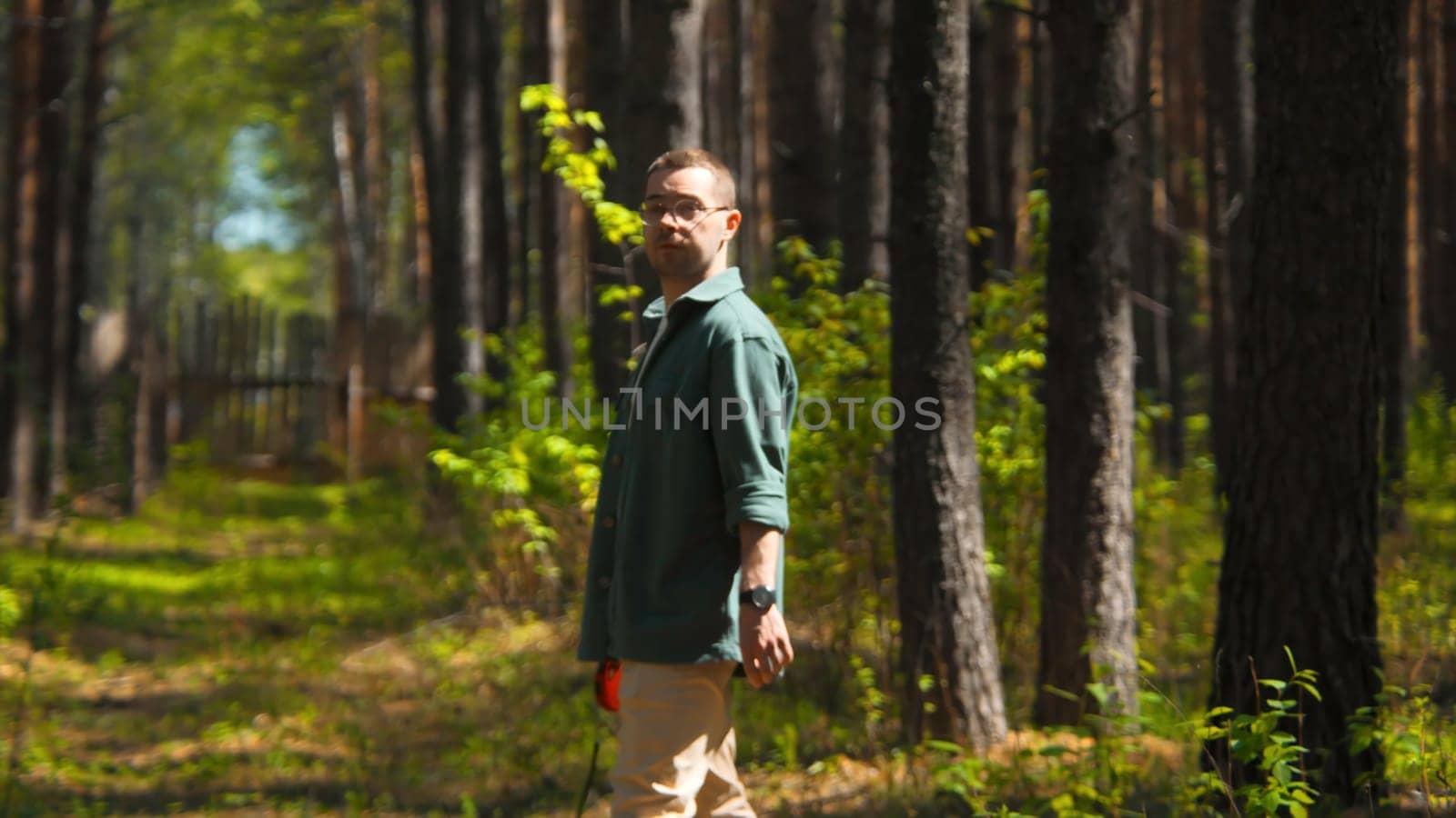 Man is looking for dog in park in summer. Stock footage. Man with leash is looking for dog in park. Man with leash looks around for dog in park in summer.