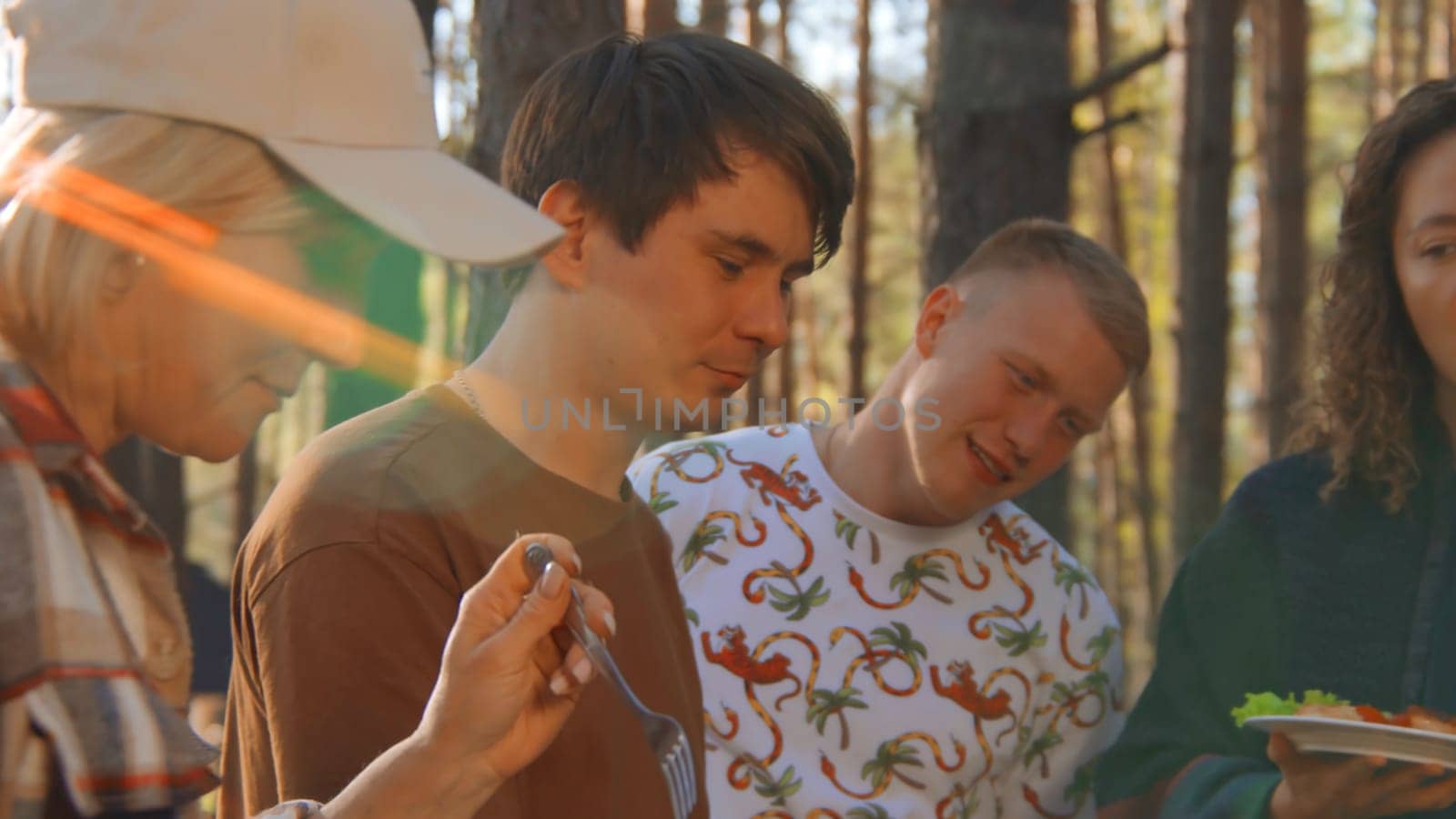 Friends communicate and eat food from barbecue in nature in summer. Stock footage. Friends are having fun talking and eating in woods on sunny summer day. Bright cheerful communication of friends in nature with barbecue by Mediawhalestock