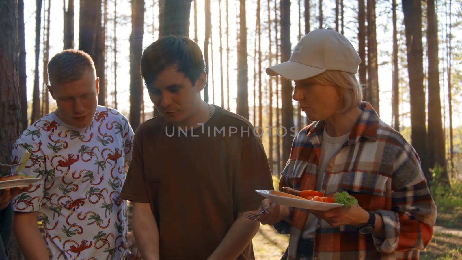 Friends eat delicious fresh food in nature. Stock footage. Friends have fun relaxing in nature and eat delicious food on grill. Friends eat from grill on background of sunlight in summer forest.