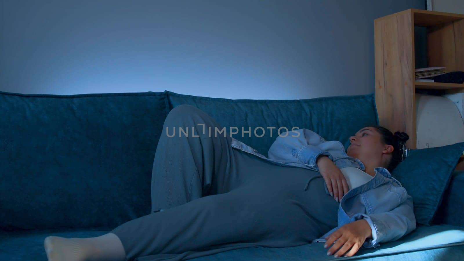 Young woman lies down on sofa with tired look. Media. Young woman lies down on sofa after hard day. Woman in tired clothes lies down on sofa at home.