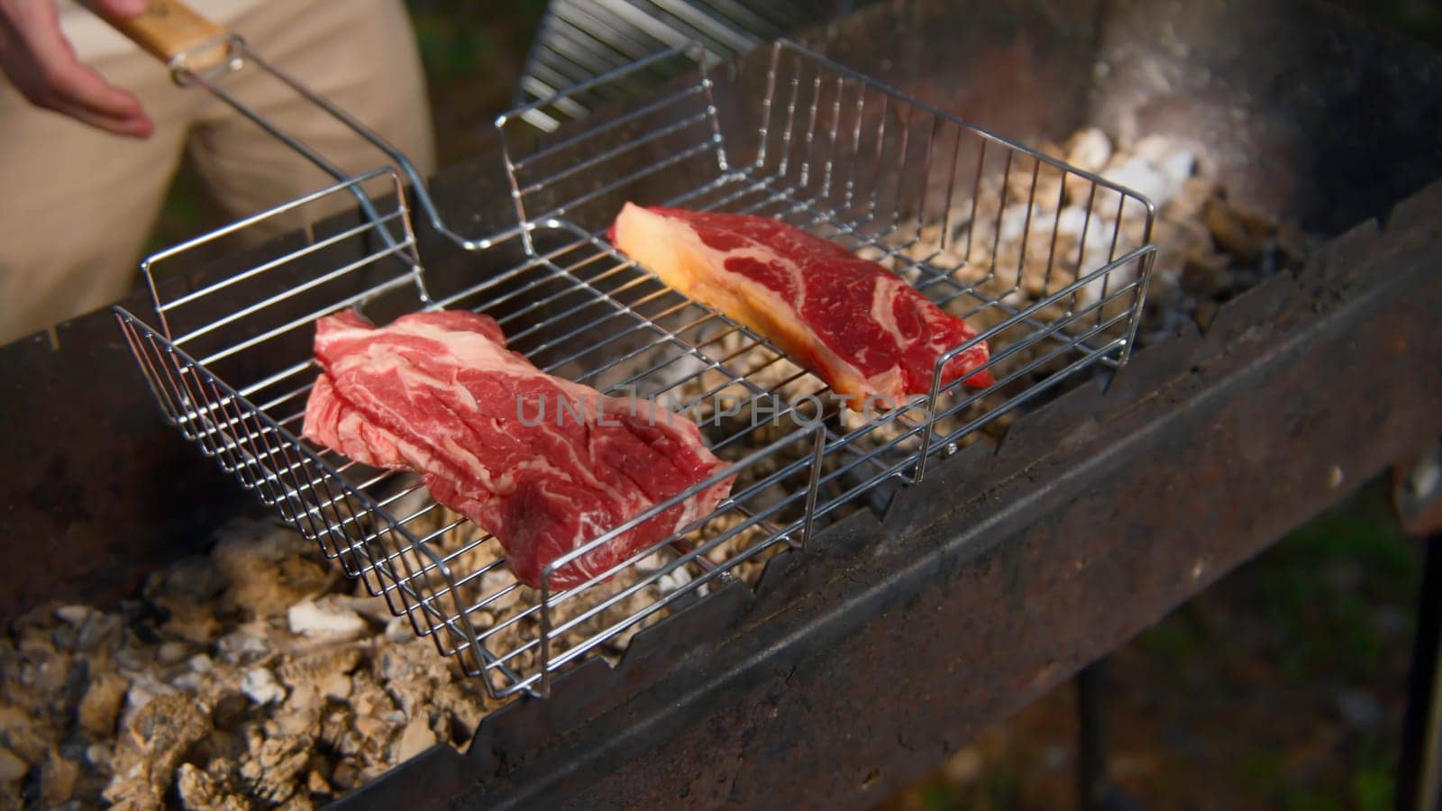 Close-up of man grilling pieces of red meat. Stock footage. Man cooks two pieces of beef or pork on grill. Man cooks meat on grill in nature in summer.