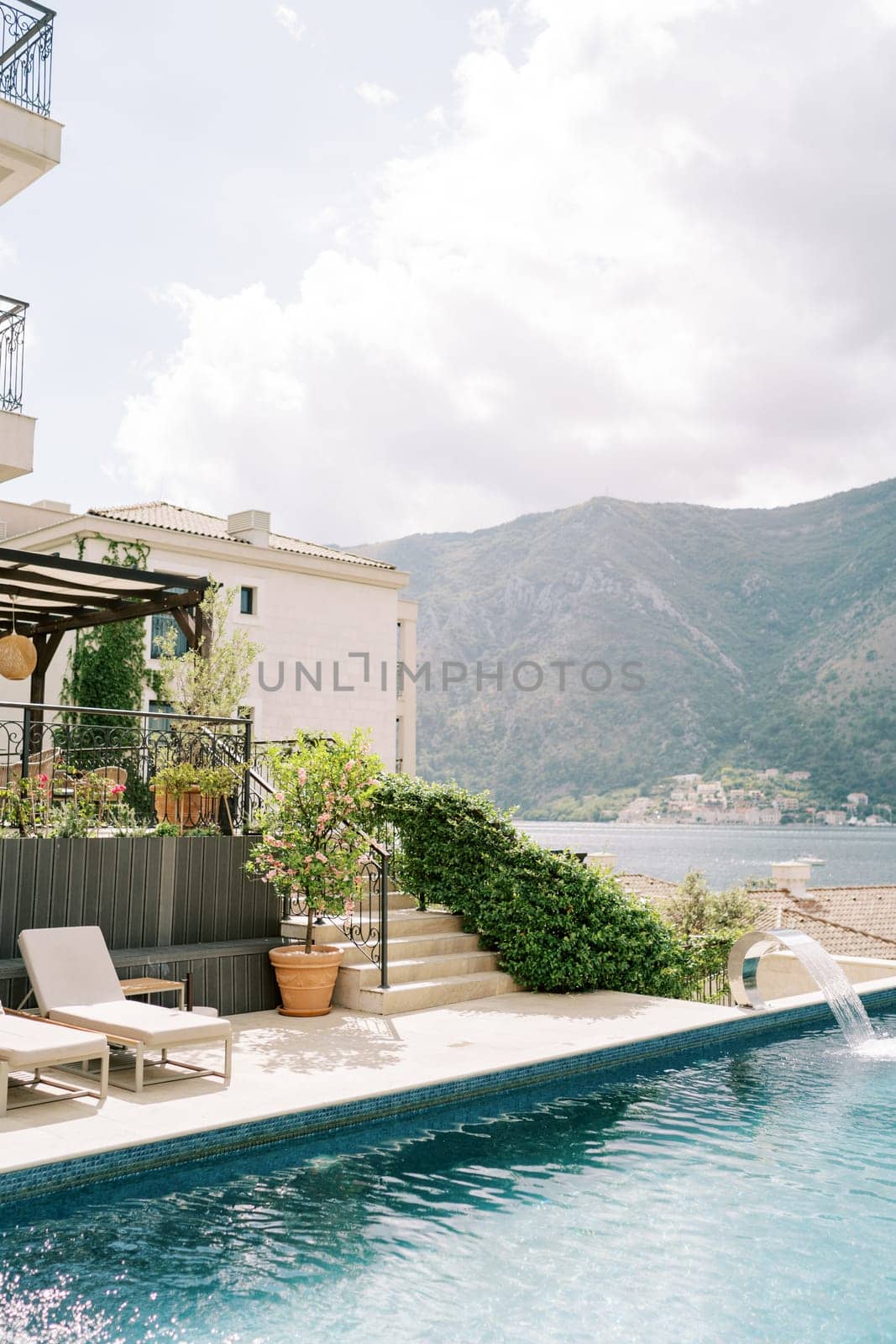 Swimming pool in the courtyard of the villa with soft sun loungers and flowering bushes in tubs on the shore. High quality photo