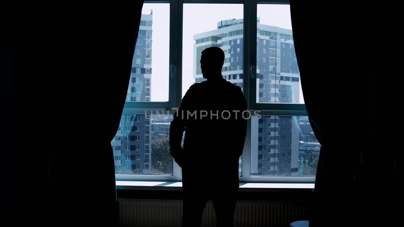 Silhouette of a business man talking on a mobile phone on the background of a window and city. Media. Successful confident businessman standing at home by the window