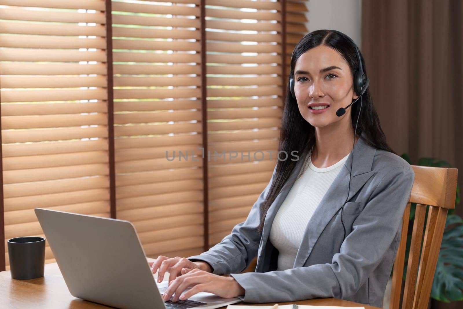 Female call center operator or customer service helpdesk staff working on workspace while talking on the headset to provide assistance for customer. Professional modern business service. Blithe