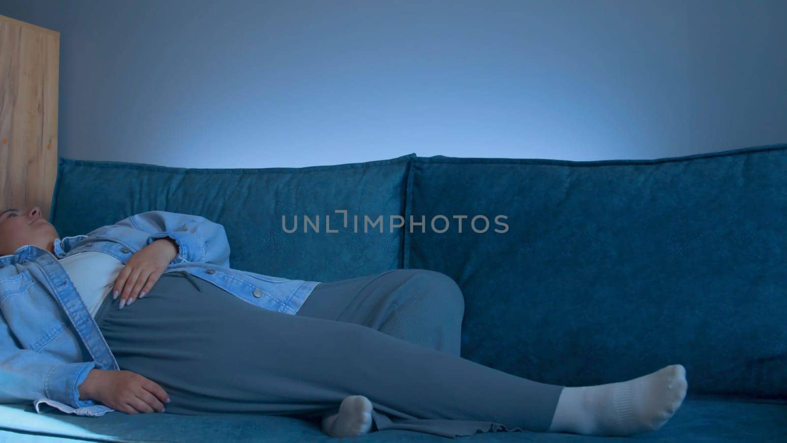 Young woman lies down on sofa with tired look. Media. Young woman lies down on sofa after hard day. Woman in tired clothes lies down on sofa at home.
