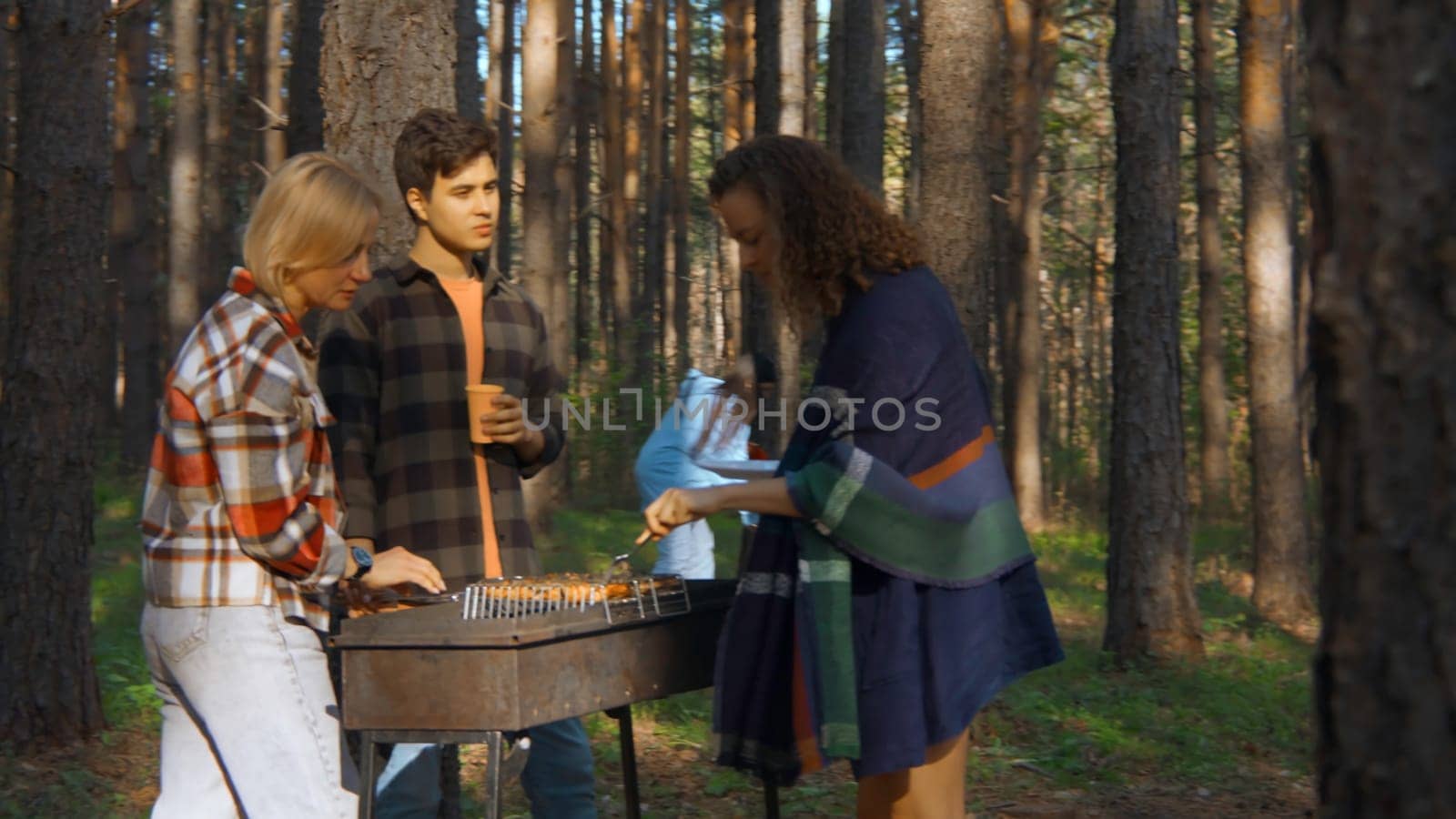 Friends cook grilled meat in forest in summer. Stock footage. Beautiful friends are relaxing in nature with barbecue in forest. Relaxing with friends in nature with barbecue on sunny summer day.