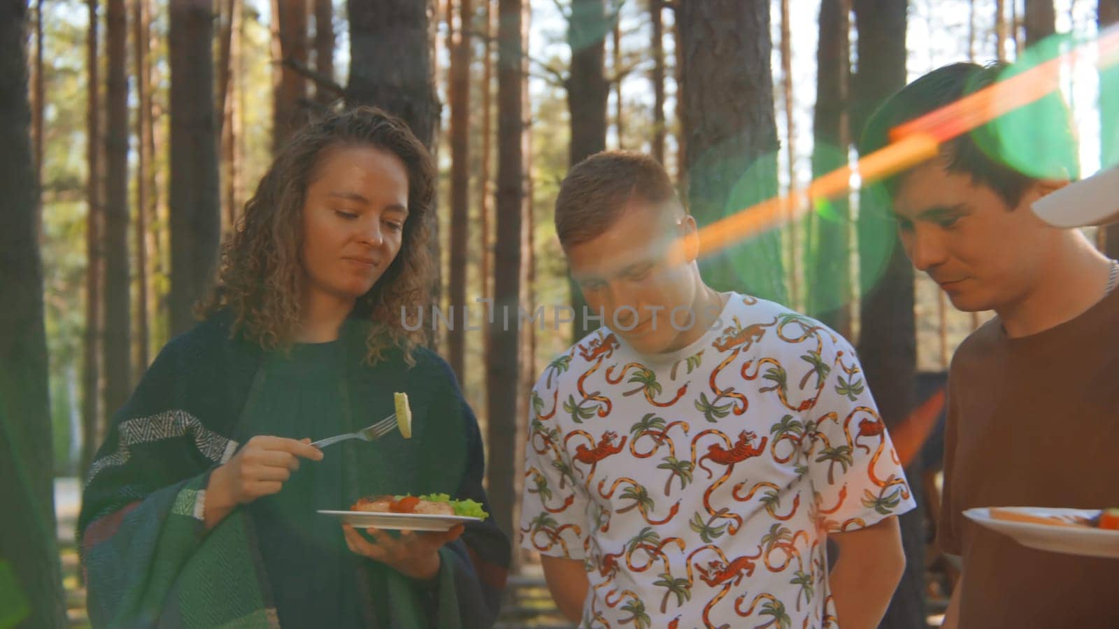 Friends communicate and eat food from barbecue in nature in summer. Stock footage. Friends are having fun talking and eating in woods on sunny summer day. Bright cheerful communication of friends in nature with barbecue by Mediawhalestock