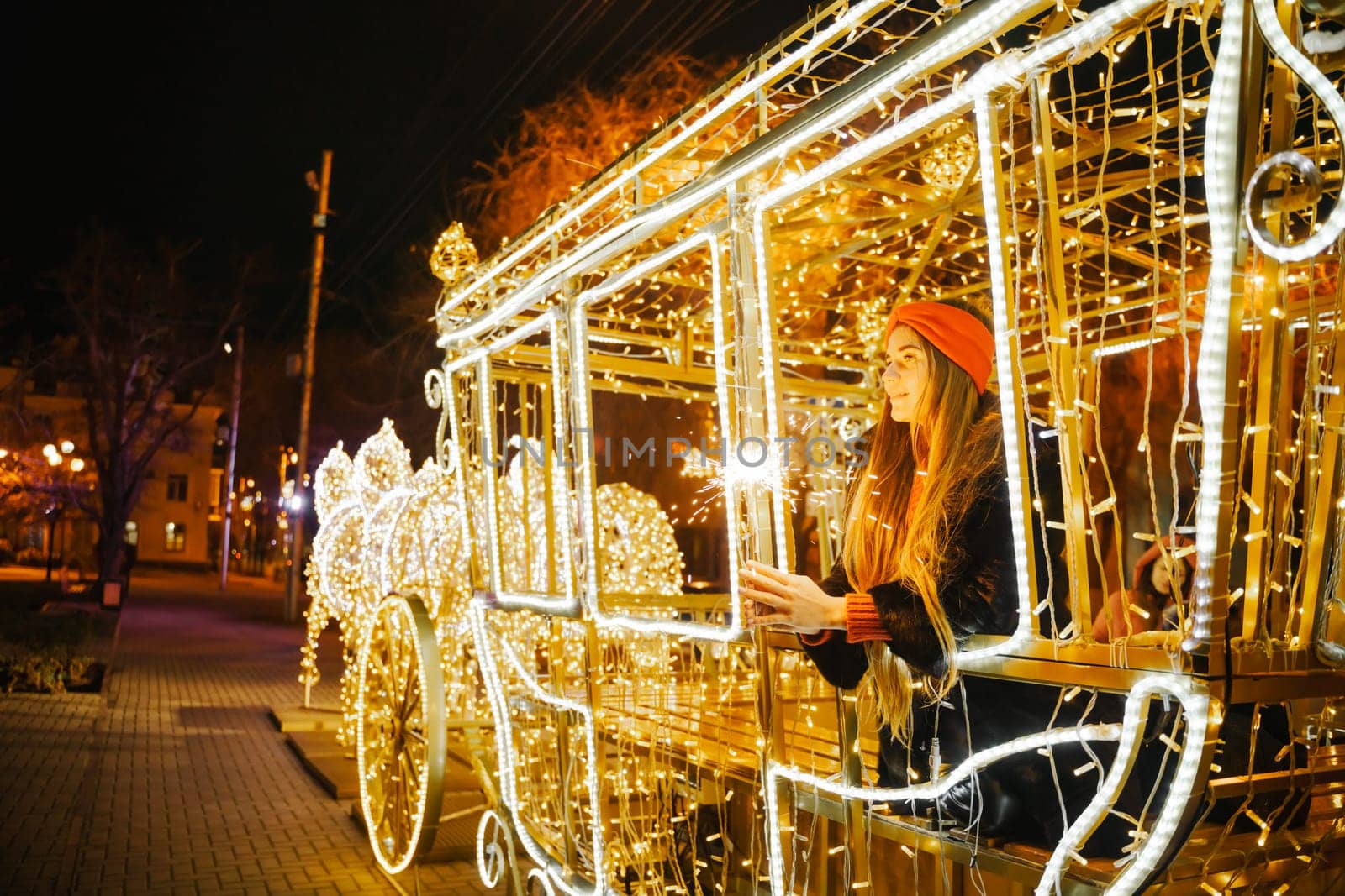 Woman holding sparkler night while celebrating Christmas outside. Dressed in a fur coat and a red headband. Blurred christmas decorations in the background. Selective focus by Matiunina