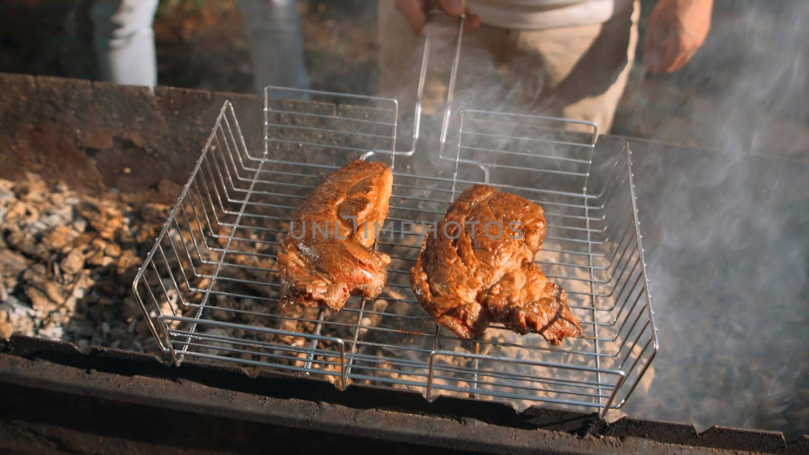 Close-up of men frying chicken on grill in forest. Stock footage. Delicious grilled chicken with barbecue on sunny summer day. Men cook chicken on grill and relax in forest.