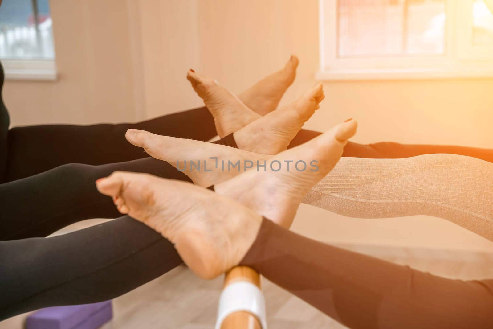 A group of six athletic women doing pilates or yoga on pink mats in front of a window in a beige loft studio interior. Teamwork, good mood and healthy lifestyle concept