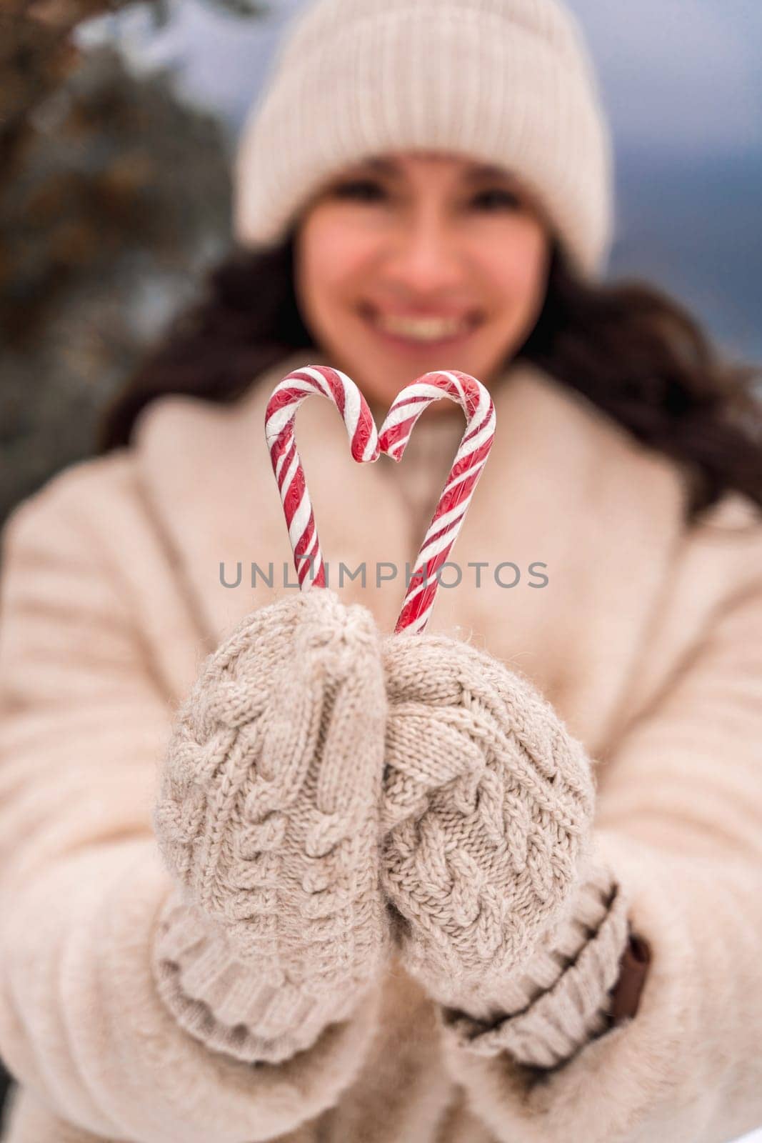 Woman candy sea. Smiling woman in knitted hat, mittens and beige coat holding lollipops candy canes in her hands in shape of heart against the backdrop of the sea