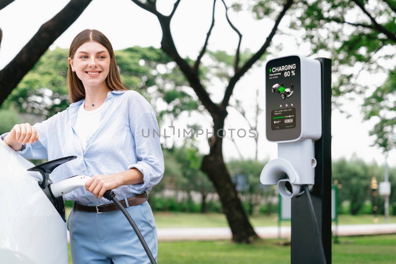 Young woman recharge EV electric vehicle battery from EV charging station. Exalt by biancoblue