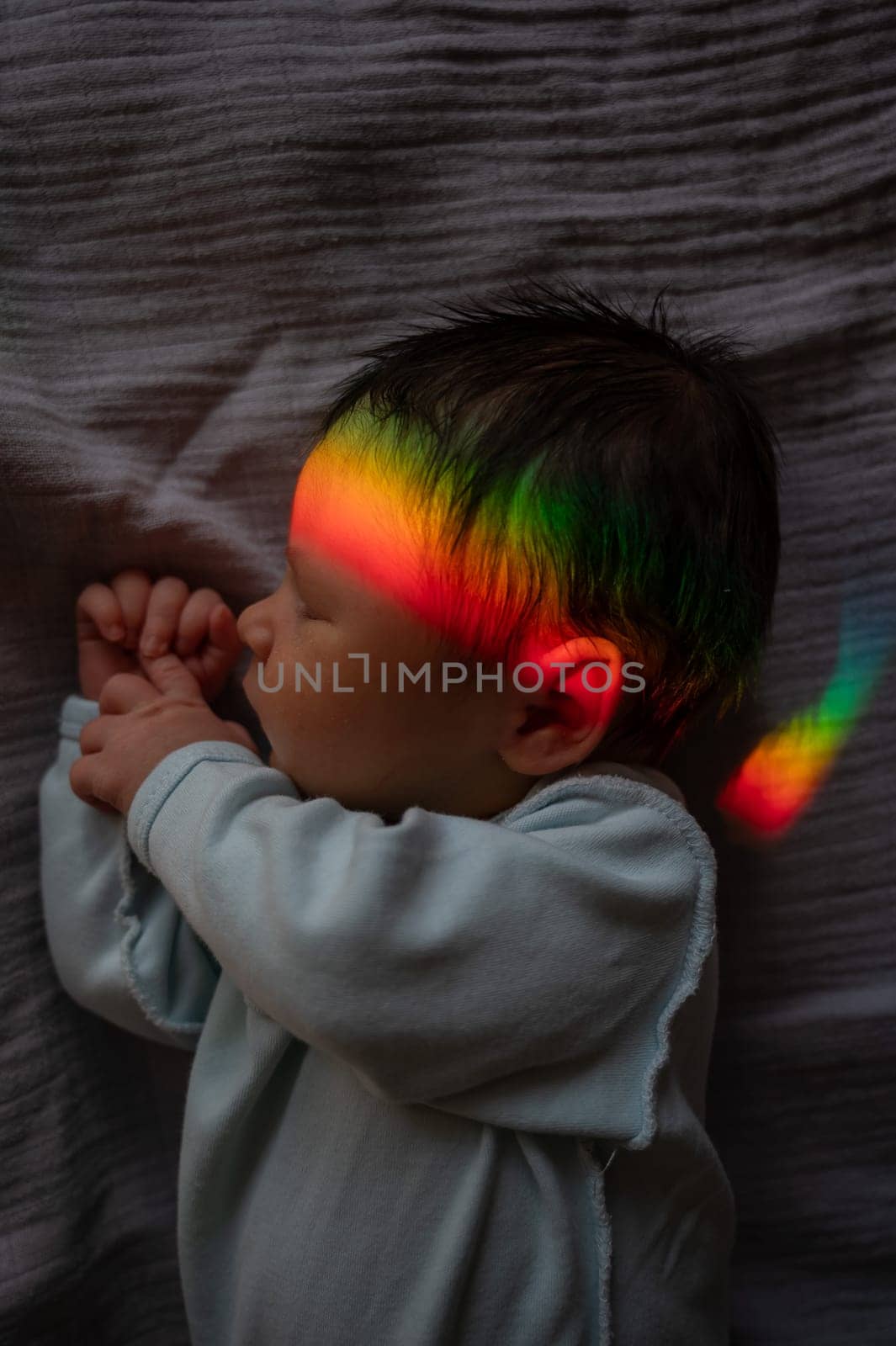 Close-up portrait of a newborn boy with a prism beam on his face. Rainbow. by mrwed54