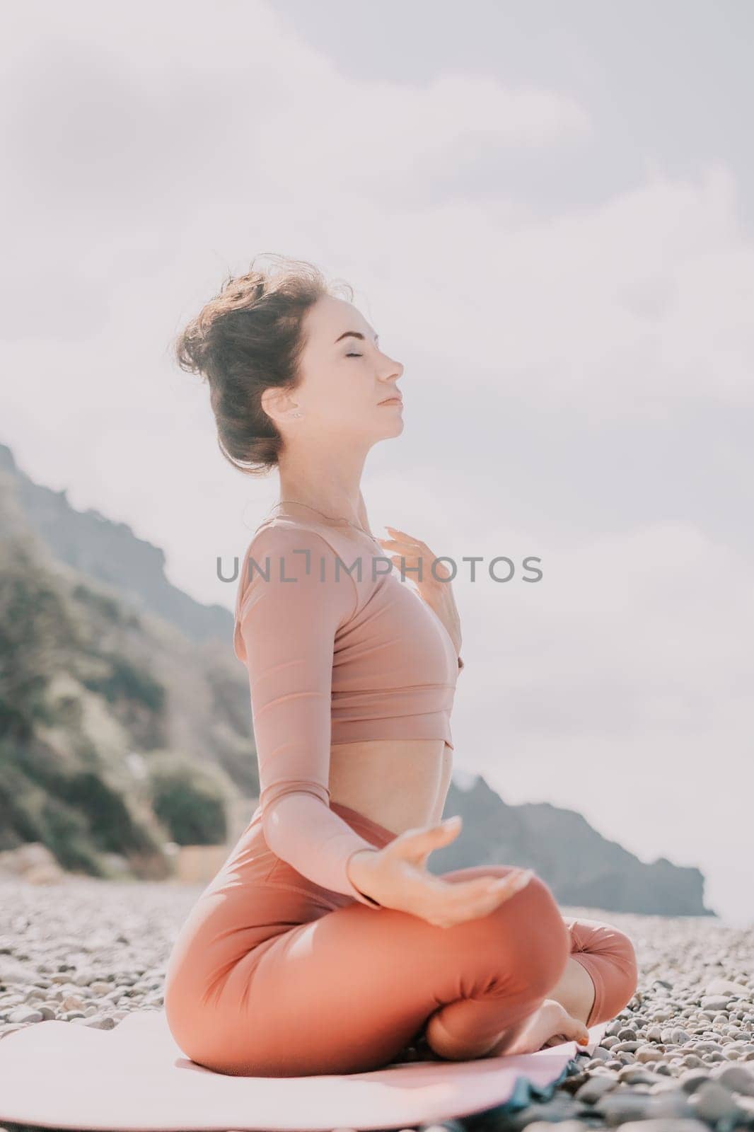 Young woman with long hair in white swimsuit and boho style braclets practicing outdoors on yoga mat by the sea on a sunset. Women's yoga fitness routine. Healthy lifestyle, harmony and meditation