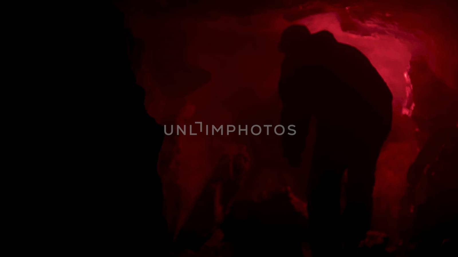 red signal flare burning inside dark natural cave making shadows on cave walls. Man got lost inside grotto and looking for help at night.