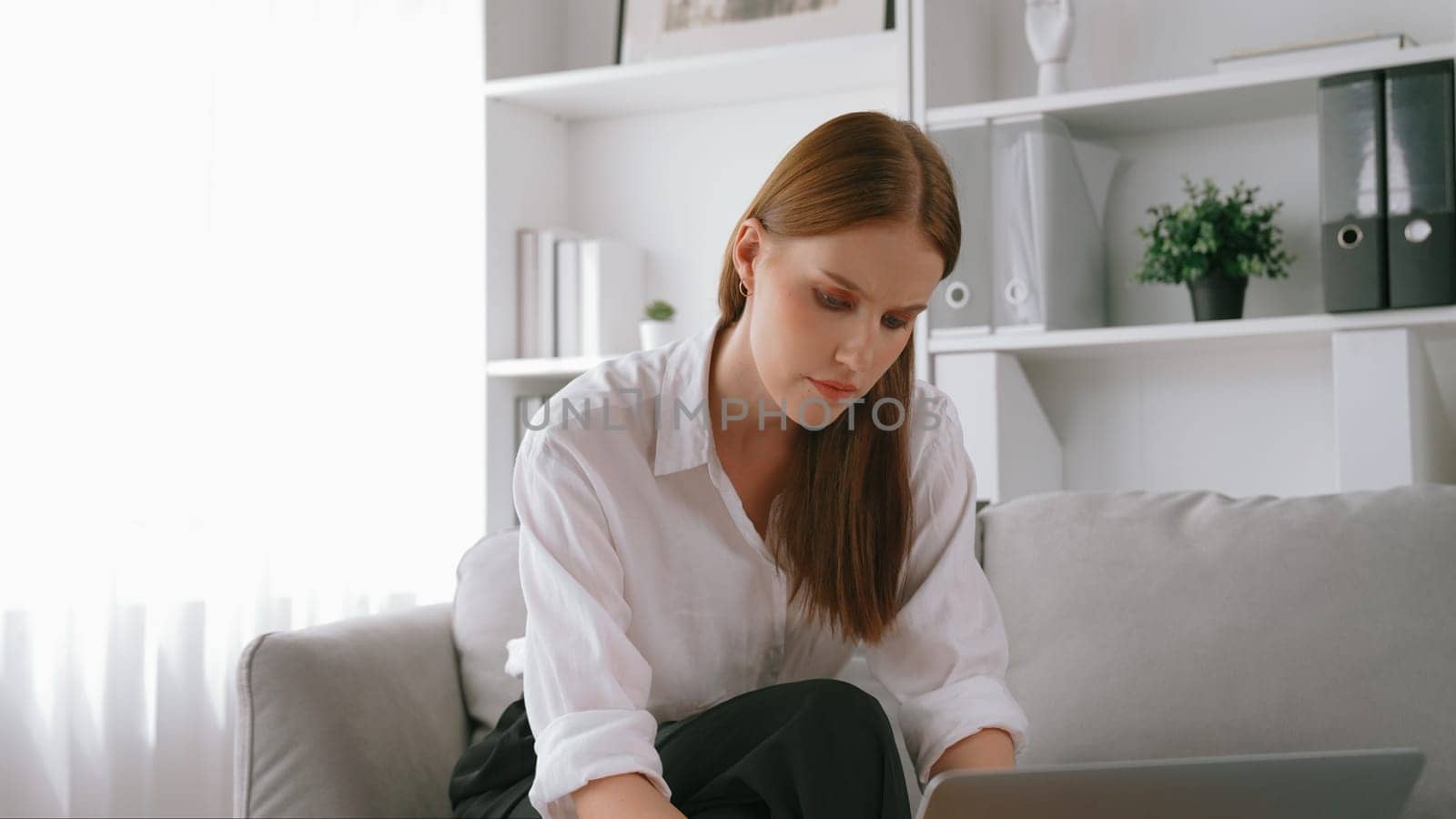 Young businesswoman sitting on the crouch using laptop computer for prim work on internet. Secretary or online content writing working at home. Remote working in domestic lifestyle