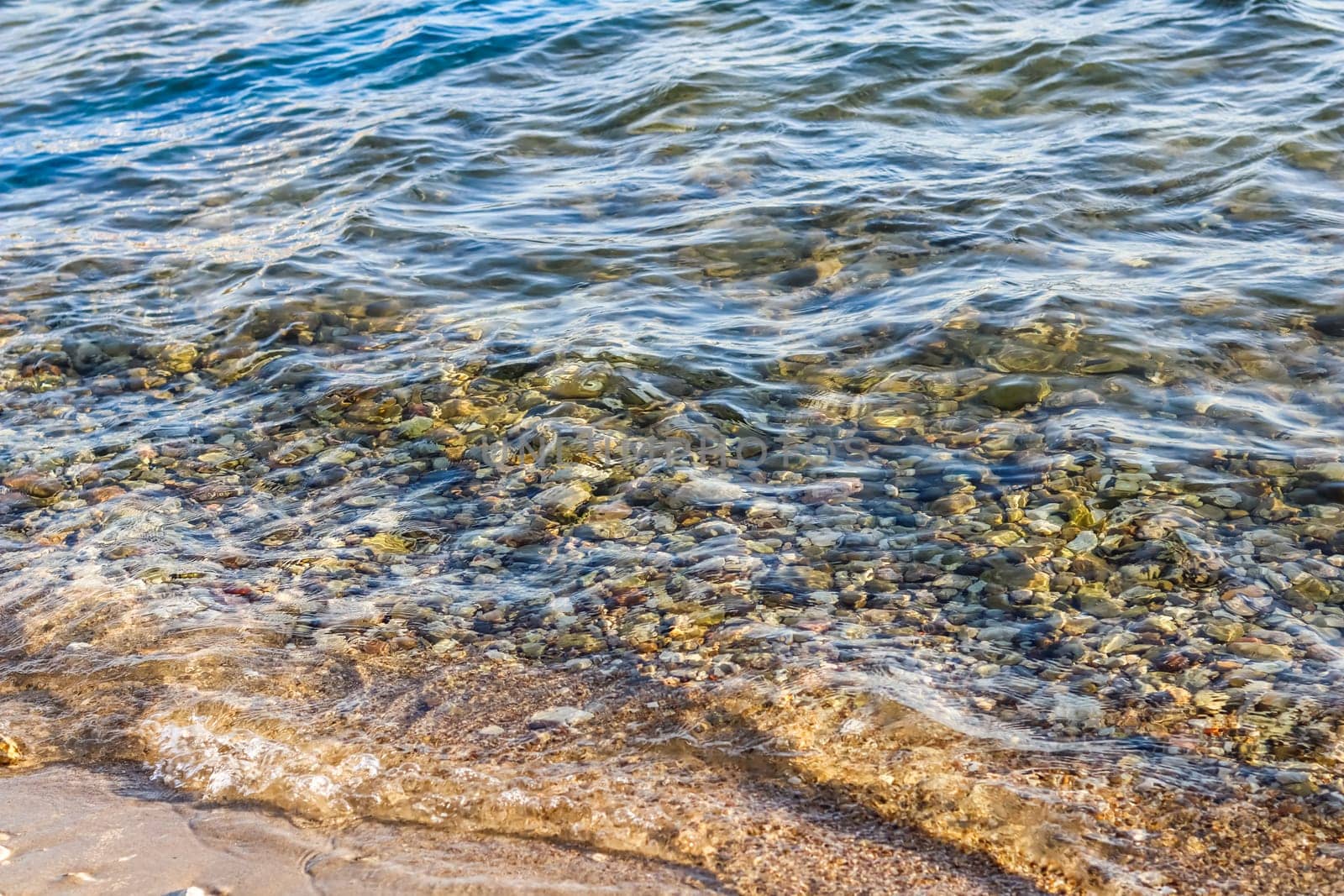 Background of sandy, stones and flowing waves on the sea beach. Summer holidays and coastal nature concept