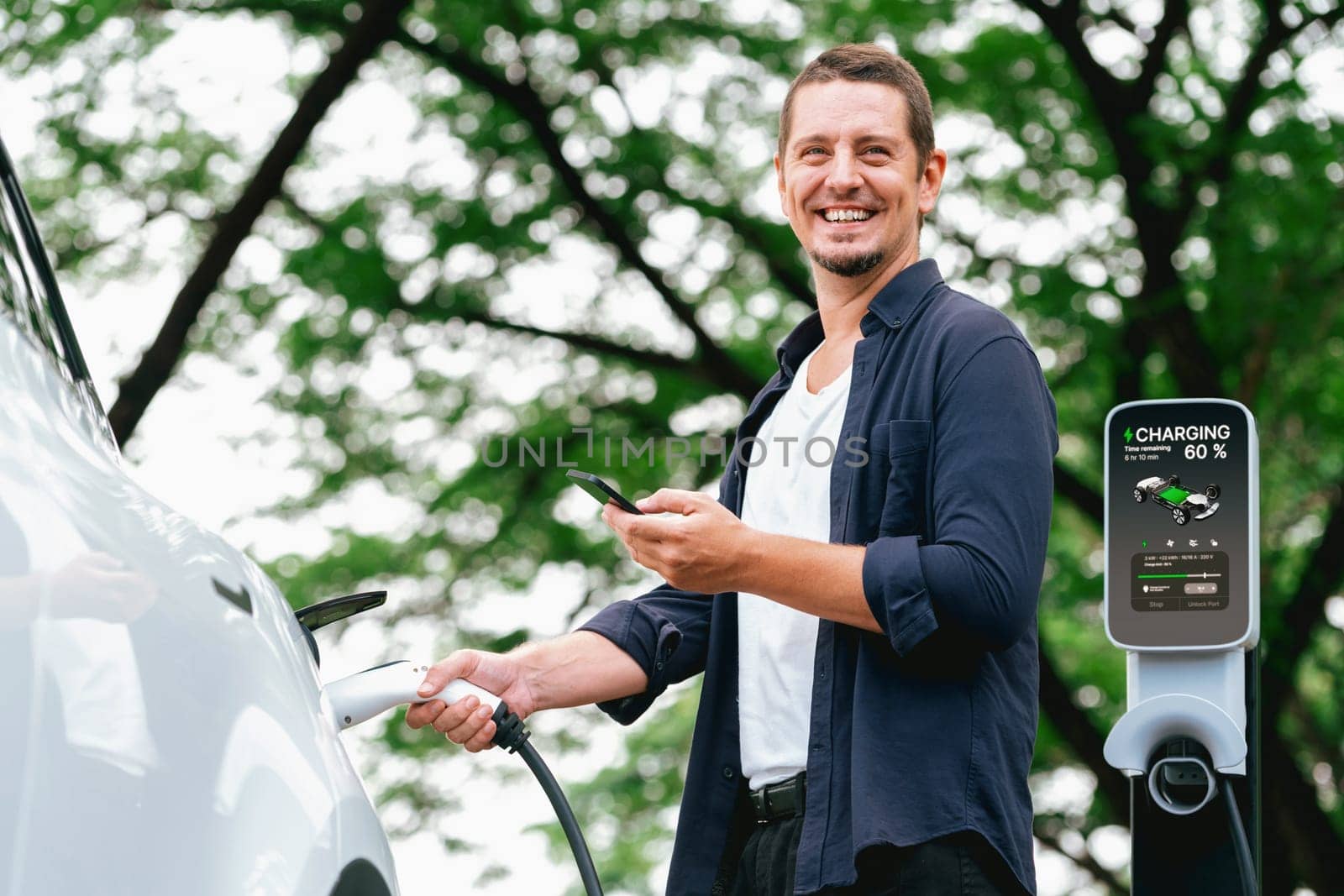 Man using smartphone online banking application to pay for electric car battery charging from EV charging station during vacation holiday road trip at national park or summer forest. Exalt