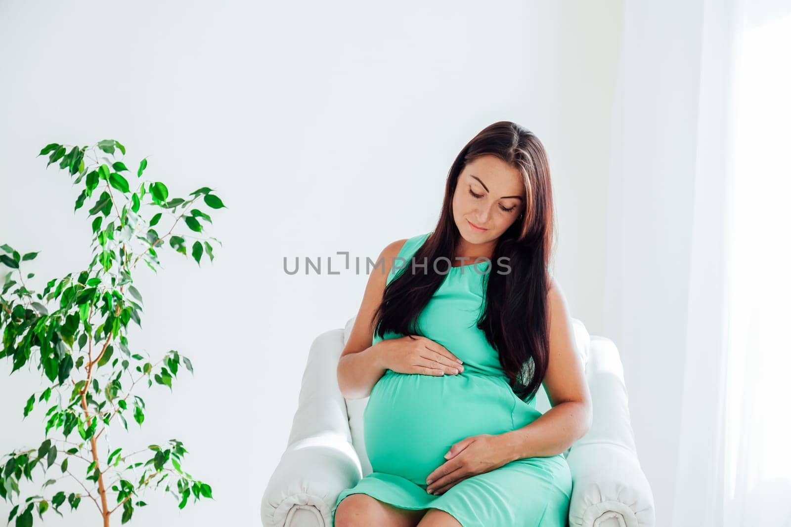 a pregnant woman before childbirth sits in white couch 1