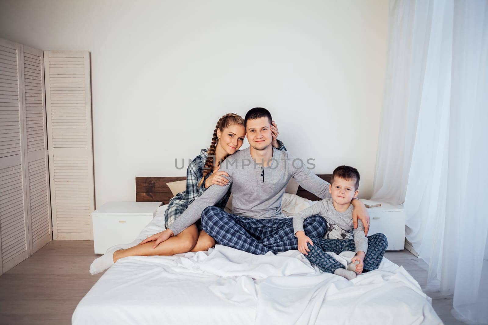 mom dad and son in the morning lying on the bed at home by Simakov
