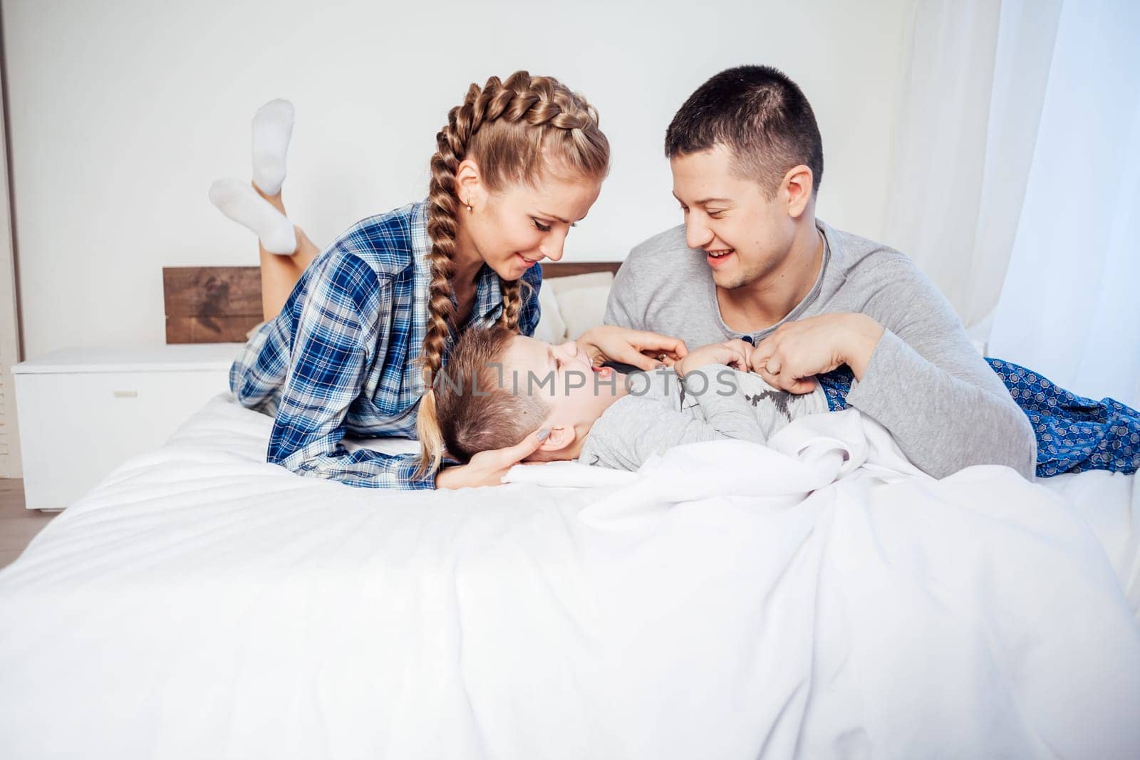 mom dad and son in the morning lying on the bed at home 1