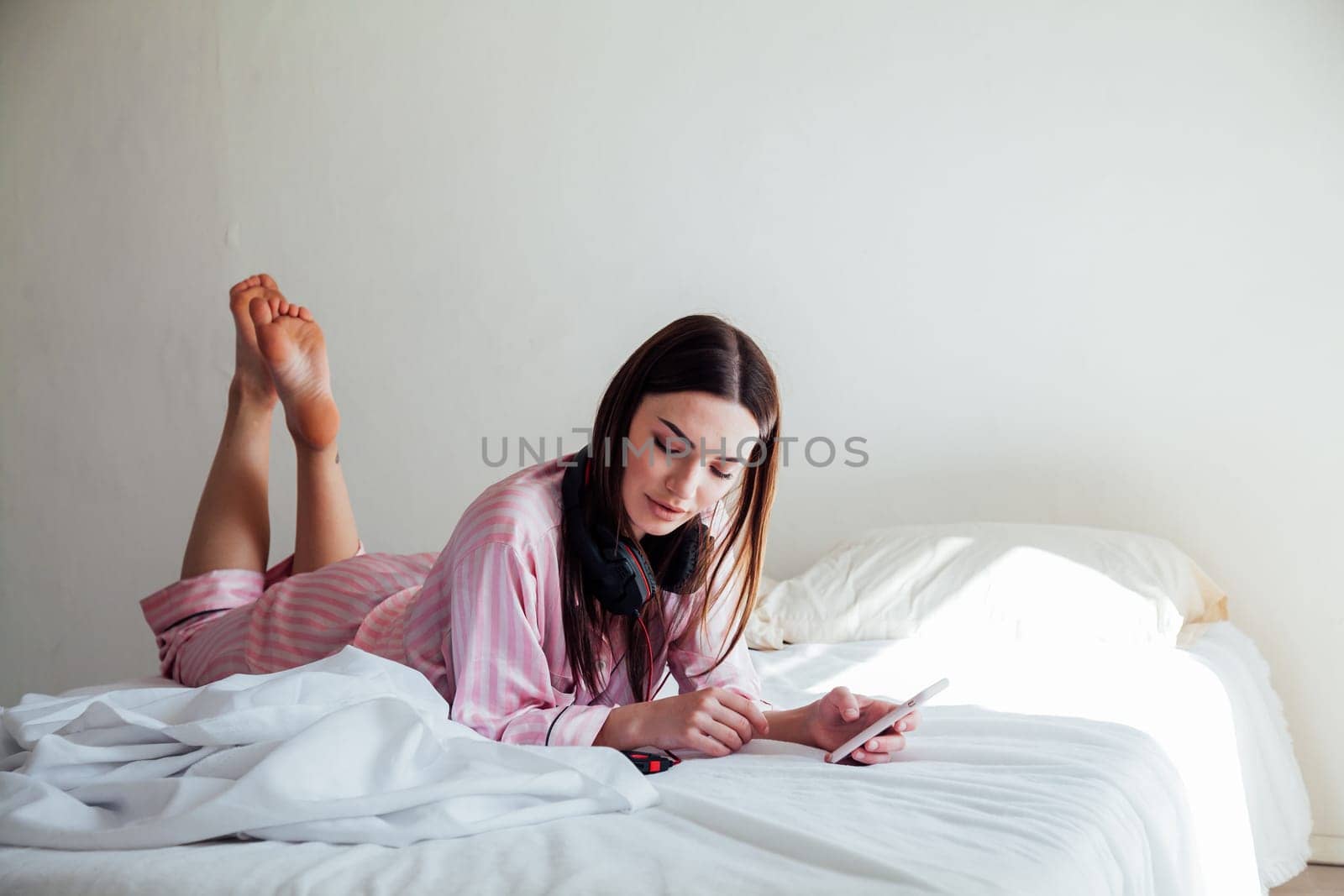 girl in pink Pajamas lying on the bed and listens to music