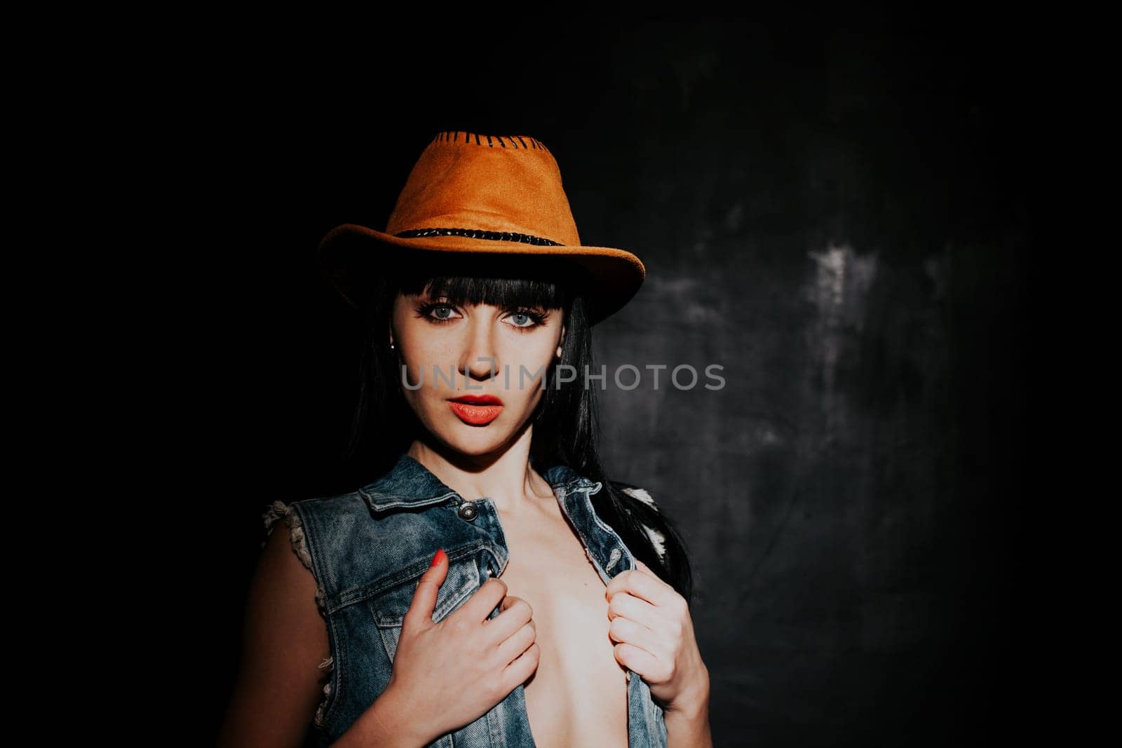 beautiful sexy girl in cowboy hat and denim waistcoat on a black background
