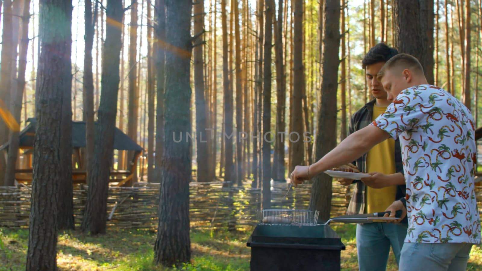 Men put barbecue on plate in nature. Stock footage. Men cooked sausages on grill in forest on sunny summer day. Men put barbecue meat on plate in nature.