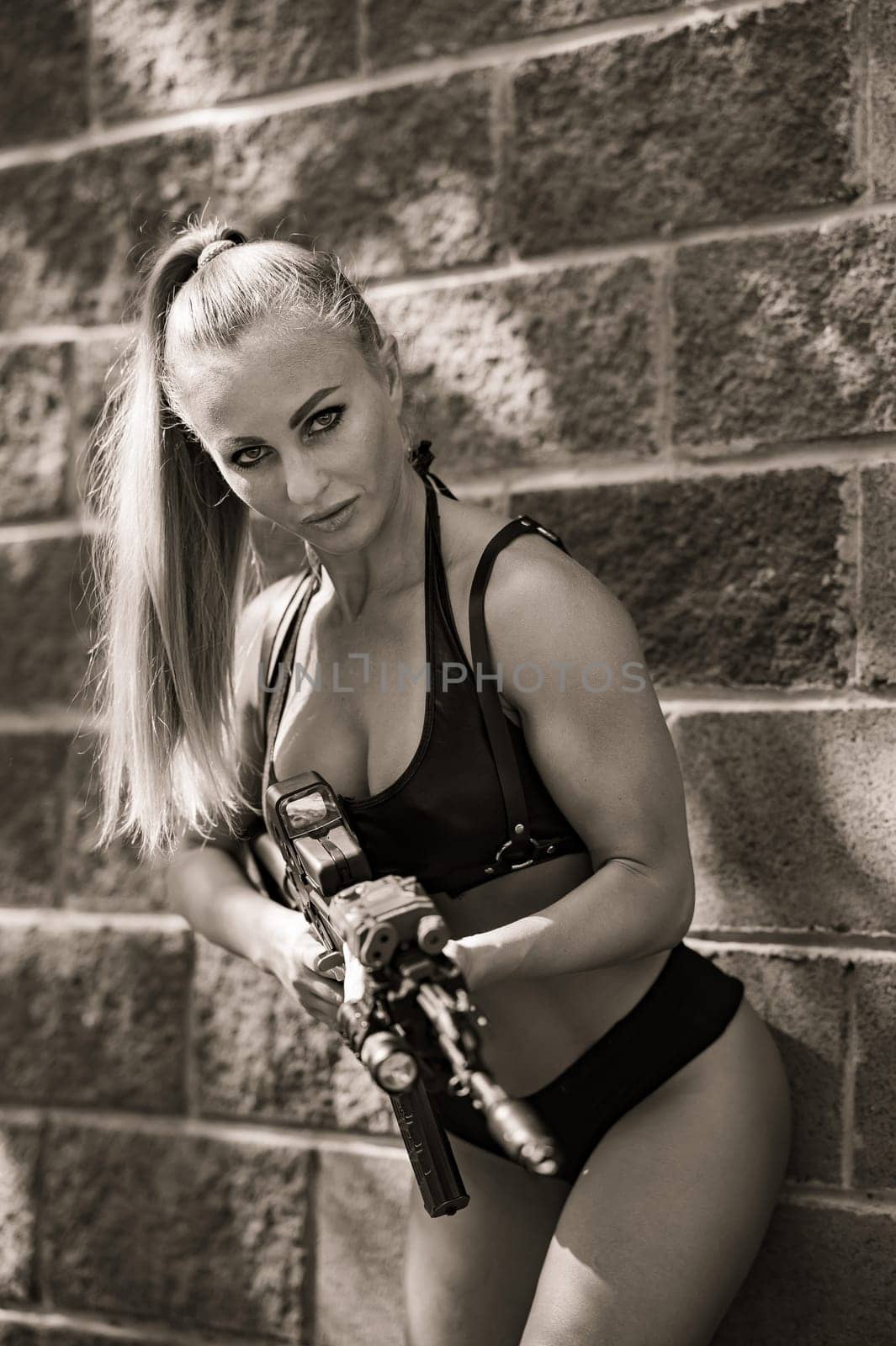 A caucasian woman in a bikini holds a machine gun against a brick wall. by mrwed54