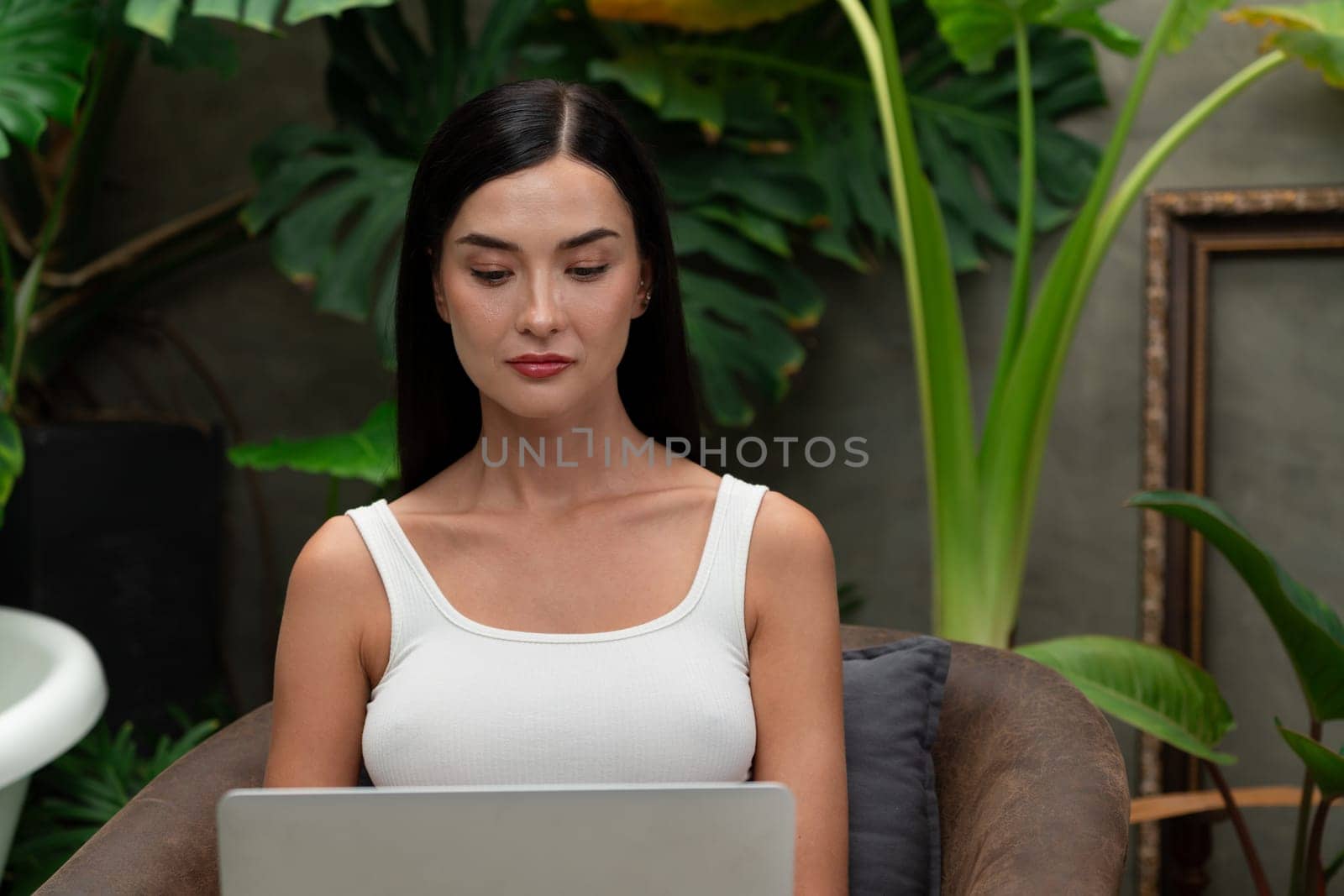 Modern young woman working remotely or relaxing in the solitude of a minimalist architectural concrete style summer exotic plant foliage garden, surrounded by tropical plants. Blithe