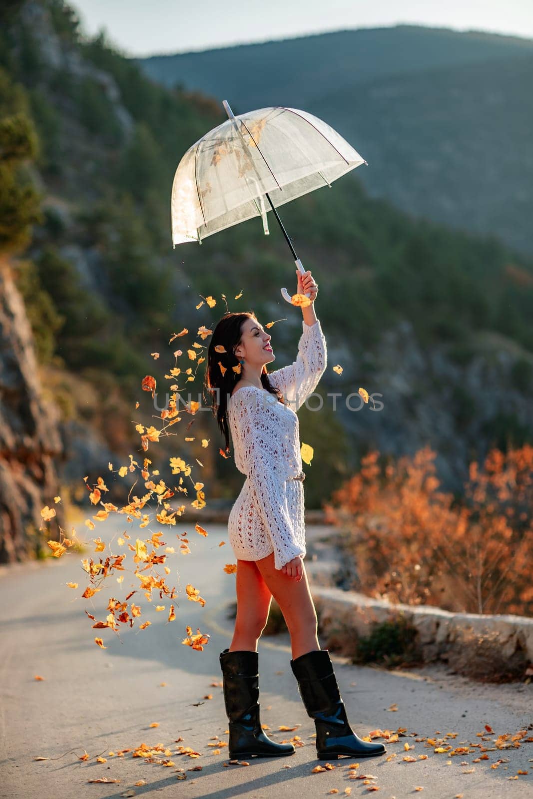 woman umbrella leaves , She holds him over her head, autumn leaves are falling out of him. Beautiful woman in a dress with an umbrella in the autumn park on the road in the mountains. by Matiunina