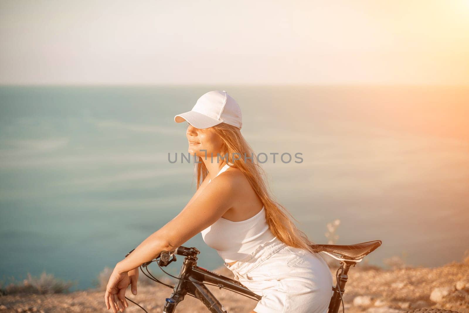 Woman travel bike sea. Happy woman cyclist sitting on her bike, enjoying the beautiful mountain and sea landscape, signifying the idea of an adventurous bike ride. by Matiunina