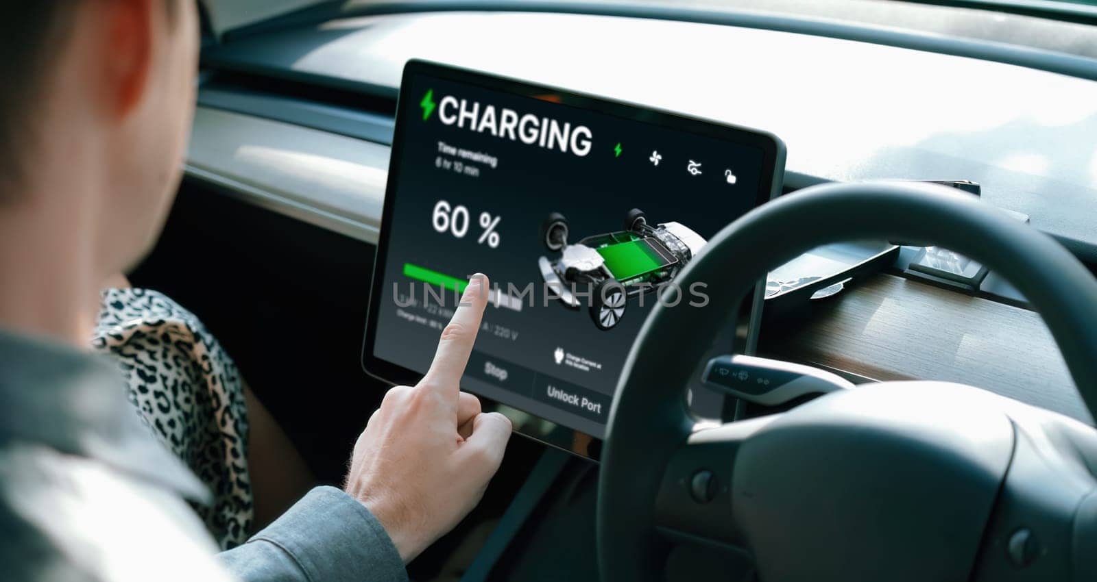 Electric car driver checks battery charging status app screen in car innards by biancoblue
