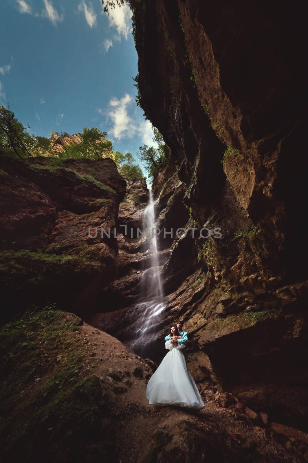Couple in love on a waterfall. Honeymoon trip. Happy couple in the mountains, high angle view of the entire mountain waterfall.