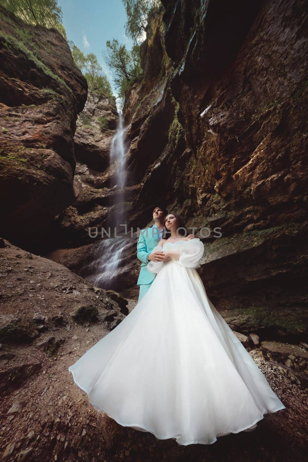 Wedding of a beautiful couple, the bride is dressed in a white dress. Stylish shooting against the backdrop of a natural landscape with a waterfall in the mountains in summer by yanik88