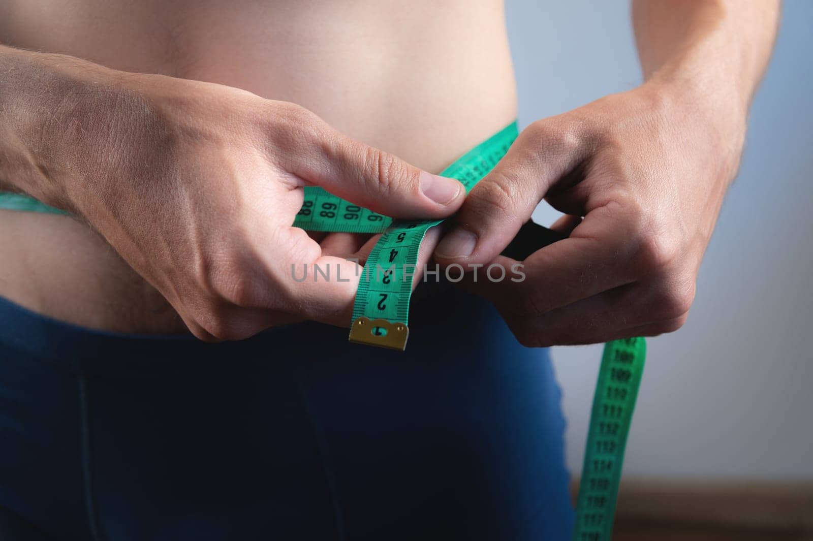 Unrecognizable athletic male athlete measuring waist with tape, checking weight loss, sports diet, healthy eating control, muscle body mass, measurements with centimeter.