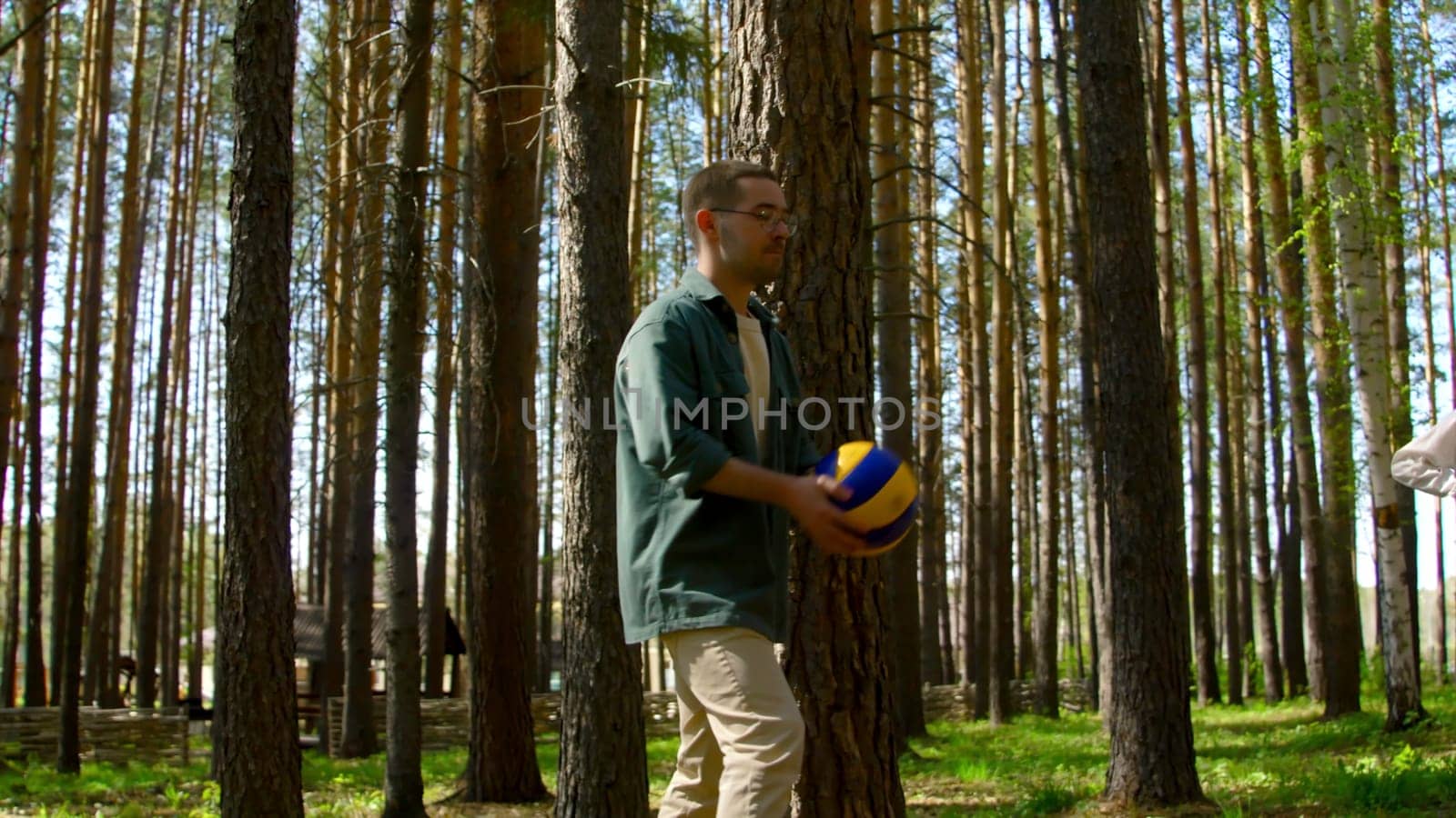 Group of friends is having fun playing volleyball. Stock footage. Friends are playing volleyball in forest clearing. Friends in circle play volleyball in forest on sunny summer day.